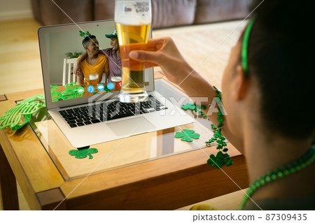 Mixed race woman holding beer having st patrick's day video call with male friends on laptop at home Mixed race woman holding beer having st patrick's day video call with male friends on laptop at home 87309435
