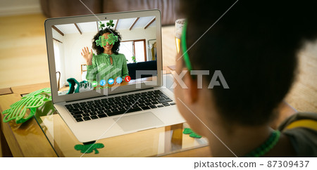 Mixed race woman having st patrick's day video call with female friend in costume on laptop at home Mixed race woman having st patrick's day video call with female friend in costume on laptop at home 87309437