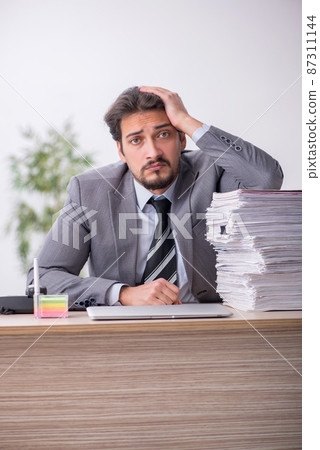 Young male employee and too much work in the office Young male employee and too much work in the office 87311144