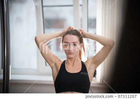 Young attractive woman in sport bra in training studio making a ponytail 87311207