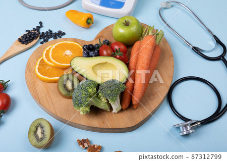High angle view of fruits and vegetables on heart shaped board over blue background, copy space High angle view of fruits and vegetables on heart shaped board over blue background, copy space 87312799