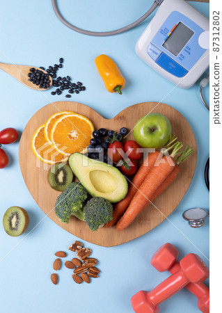 Overhead view of vegetables and fruits on heart shape cutting board over blue background, copy space Overhead view of vegetables and fruits on heart shape cutting board over blue background, copy space 87312802