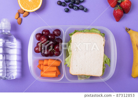 Overhead view of healthy food and tiffin box by water bottle over purple background, copy space 87312853