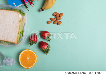 Overhead view of fruits and sandwiches in tiffin box on green background with copy space Overhead view of fruits and sandwiches in tiffin box on green background with copy space 87312870