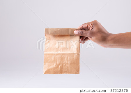 Cropped image of african american person hand holding paper lunch bag against white background Cropped image of african american person hand holding paper lunch bag against white background 87312876