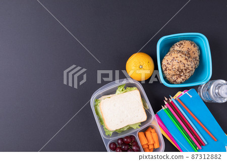 Directly above shot of healthy food and tiffin with school supplies on black background, copy space 87312882