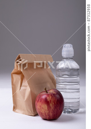 Close-up of brown paper lunch bag with apple and water bottle on table against gray background 87312938
