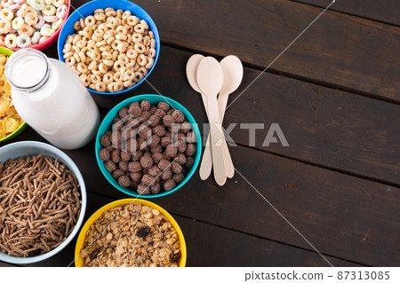 Various breakfast cereals in bowls around milk bottle on wooden table Various breakfast cereals in bowls around milk bottle on wooden table 87313085