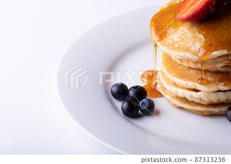Close-up of dripping syrup over stacked pancakes with berry fruits in plate on white background Close-up of dripping syrup over stacked pancakes with berry fruits in plate on white background 87313236