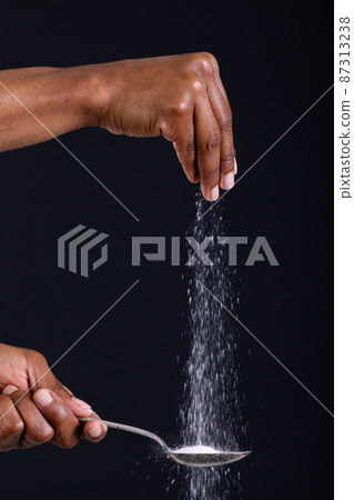 Cropped hand of african american man sprinkling seasoning on spoon against black background Cropped hand of african american man sprinkling seasoning on spoon against black background 87313238
