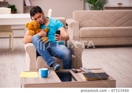 Young man sitting with bear toy at home Young man sitting with bear toy at home 87313480