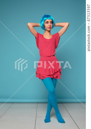 Close up of a flirtatious female model on blue background wearing a blue wig. Pretty glamorous woman pink hair charm sweets lifestyle. Baby doll 87313597