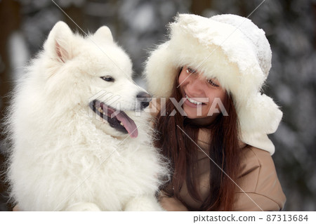 Happy young woman in winter, holds in her arms and plays in the snow with her pet dog 87313684