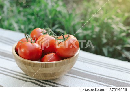 A lot of red tomatoes in a wooden plate, on a background of greens. 87314956