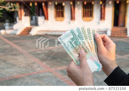 Cropped shot view of someone holding banknotes of Laos kip money (100,000 kip) the national currency of Laos. Cropped shot view of someone holding banknotes of Laos kip money (100,000 kip) the national currency of Laos. 87315108