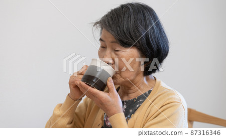 An old woman in her 80s drinking coffee like tea 87316346