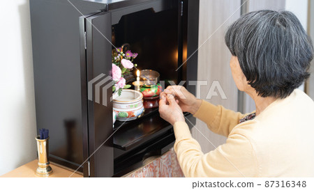 An old woman in her 80s giving incense sticks to a Buddhist altar 87316348