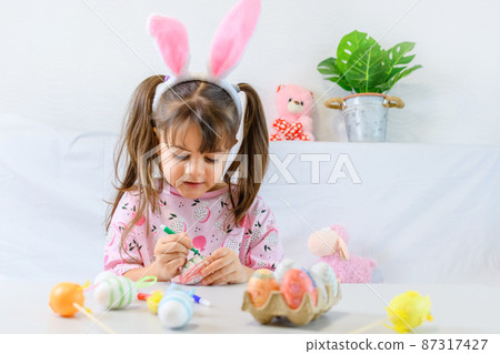 Happy little girl with bunny ears painting the egg with fiberpen, preparing for Happy Easter day. Preparing handmade . Happy little girl with bunny ears painting the egg with fiberpen, preparing for Happy Easter day. Preparing handmade . 87317427