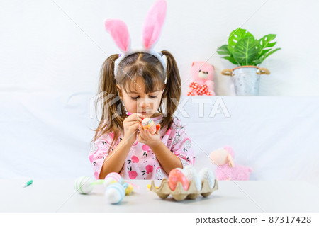 Happy little girl with bunny ears painting the egg with fiberpen, preparing for Happy Easter day. Preparing handmade . Happy little girl with bunny ears painting the egg with fiberpen, preparing for Happy Easter day. Preparing handmade . 87317428