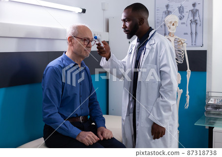 African american physician doctor putting infrared thermometer on senior man patient foredhead African american physician doctor putting infrared thermometer on senior man patient foredhead 87318738