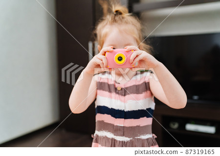 a funny little girl takes a photo on a little pink toy camera.  87319165