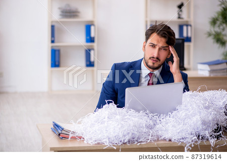 Young male employee and a lot of cut papers in the office Young male employee and a lot of cut papers in the office 87319614