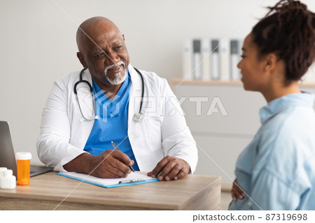 Male doctor consulting young smiling pregnant woman, writing record Male doctor consulting young smiling pregnant woman, writing record 87319698