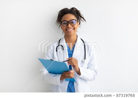 Portrait of black doctor posing with clipboard at white studio 87319768