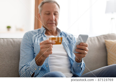 Mature man using phone and credit card at home 87319769