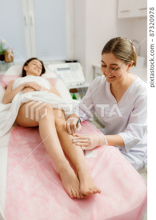 Dermatologist doing hair removal treatment on patient's leg with electrolysis. Depilation and beauty concept, hands doing electro-epilation. Doctor working in cosmetic medical cabinet. 87320978