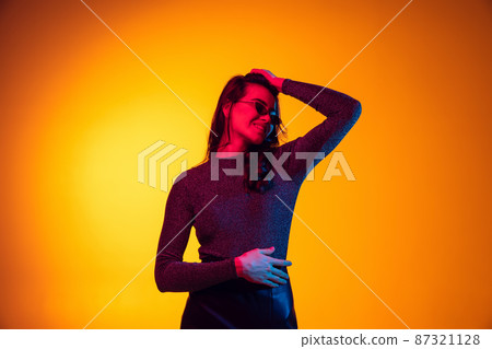 Beautiful young excited girl, student with long dark hair isolated on gradient yellow background in neon light. Concept of emotions, youth 87321128