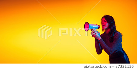 Beautiful young excited girl, student shouting at megaphone isolated on gradient yellow background in neon light. Concept of emotions, youth Beautiful young excited girl, student shouting at megaphone isolated on gradient yellow background in neon light. Concept of emotions, youth 87321136