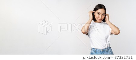 Portrait of cute, beautiful asian woman touching her new short haircut, showing hairstyle, smiling happy at camera, standing over white background Portrait of cute, beautiful asian woman touching her new short haircut, showing hairstyle, smiling happy at camera, standing over white background 87321731