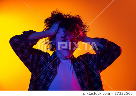 Portrait of young curly man in checkered shirt touching head in headache isolated over gradient yellow orange background in neon light 87322503