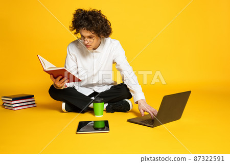 Portrait of young man, concentrated student studing, preparing for exams, reading isolated over yellow studio background Portrait of young man, concentrated student studing, preparing for exams, reading isolated over yellow studio background 87322591