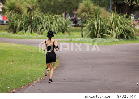 一個健康的女人早上在綠樹環繞的公園裡跑步 87323447