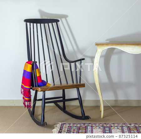 Classic dark brown rocking chair and old style vintage table on background of off white wall 87325114