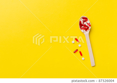 Vitamin capsules in a wooden spoon on a colored background. Pills served as a healthy meal. Drugs, pharmacy, medicine or medical healthycare concept 87326004