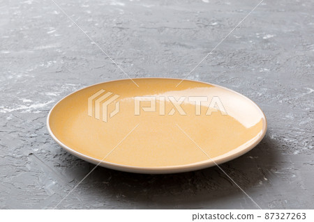 Perspective view of empty orange plate on cement background. Empty space for your design Perspective view of empty orange plate on cement background. Empty space for your design 87327263