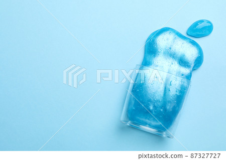 Overturned plastic container with bright slime on light blue background, top view. Space for text 87327727
