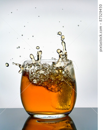 Creative splashes of whisky in a glass against a white background. 87329450