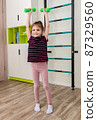 A little girl goes in for sports in her room. 87329560
