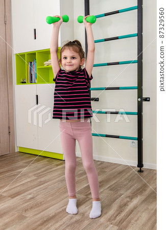 A little girl goes in for sports in her room. 87329560