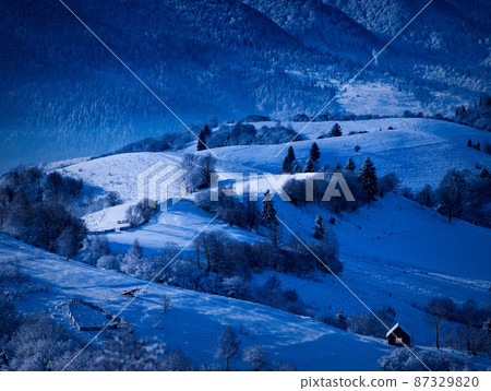 night is coming, old house covered with snow on the background of the forest 87329820