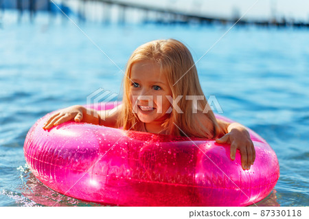 Little girl with pink inflatable circle bathing in sea 87330118