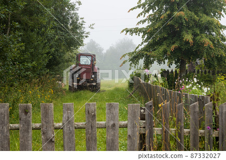 Agricultural tractor near trees and a wooden fence 87332027
