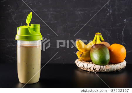 Milk protein shake and fruit on a plate. Cocktail in a shaker on a dark background. Milk protein shake and fruit on a plate. Cocktail in a shaker on a dark background. 87332167