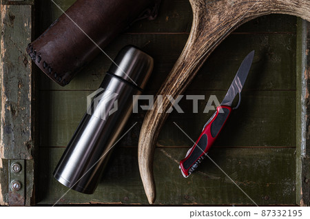 Army knife and thermos. Army knife with red handle. Knife and moose horn. Military composition. Flat lay. 87332195