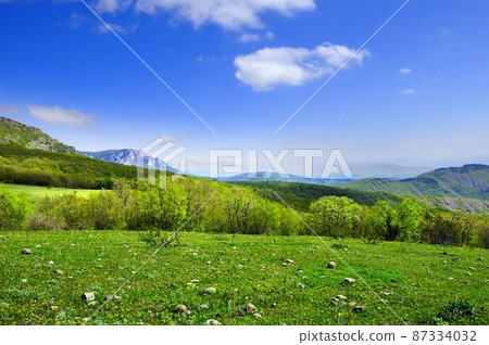 Horizontal background with a magnificent landscape of the Crimean Peninsula. Top view of the mountains covered with lush greenery and the thick clouds below the peaks. Clear blue sky. Copy space. Horizontal background with a magnificent landscape of the Crimean Peninsula. Top view of the mountains covered with lush greenery and the thick clouds below the peaks. Clear blue sky. Copy space. 87334032