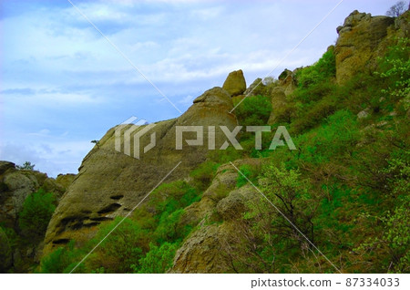 Horizontal background with a magnificent landscape of the Crimean Peninsula. Top view of the mountains covered with lush greenery and the thick clouds below the peaks. Clear blue sky. Copy space. 87334033